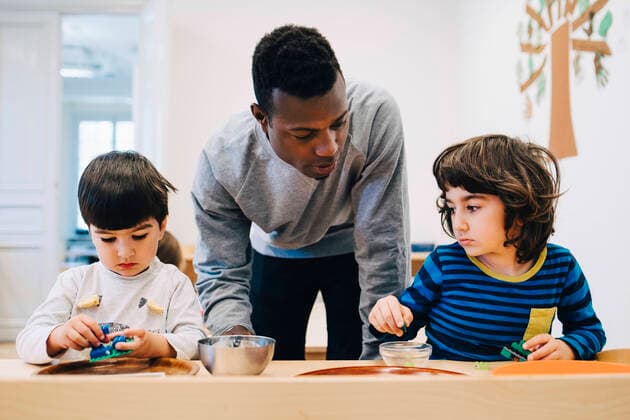 Male teacher looking at students playing with toys at table in child care classroom , model released, property released Copyright: xMaskotx , MA65873