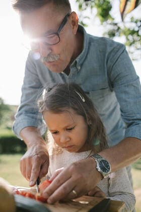 Grandfather teaching granddaughter to cut tomato at table in backyard , model released, property released Copyright: xMaskotx , MA67082