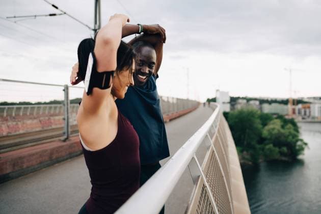 IMAGO Creative, Jahreszeit Sommer, Sommer in der Stadt Smiling male and female athletes stretching hands on footbridge over sea against sky , model released Copyright: xMaskotx , MA67270