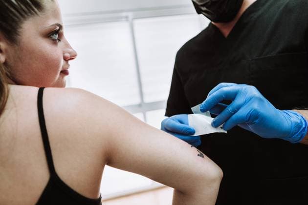 Crop anonymous male tattooist in latex gloves wiping freshly made tattoo on arm of female client with napkin while working in salon, Model released, Property released Copyright: xIvanxPujolx MR