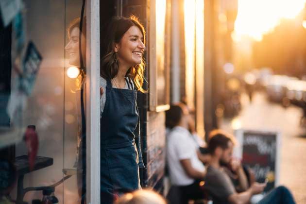 IMAGO Creative, Jahreszeit Sommer, Sommer in der Stadt IMAGO Creative, Frühling, Start der Straßencafe-Saison Smiling female owner looking away while standing at entrance of deli , model released, property released Copyright: xMaskotx , MA67638
