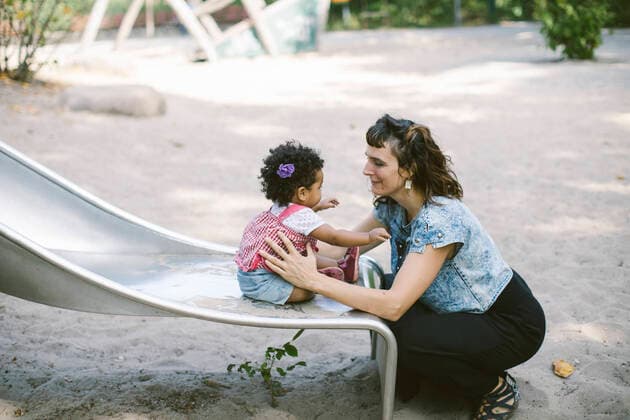 Side view of mother supporting daughter sitting on slide at playground , model released Copyright: xMaskotx , MA67888