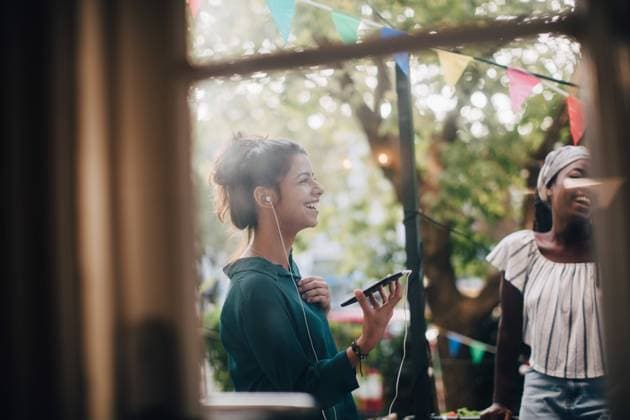 Happy young woman talking through earphones while standing with friend in balcony during party , model released, property released Copyright: xMaskotx , MA68027