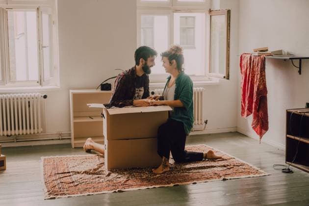 IMAGO Creative: Neue Aussichten Cheerful couple laughing while sitting next to opened cardboard box in modern apartment, Model released Copyright: xJakexJakabx MR