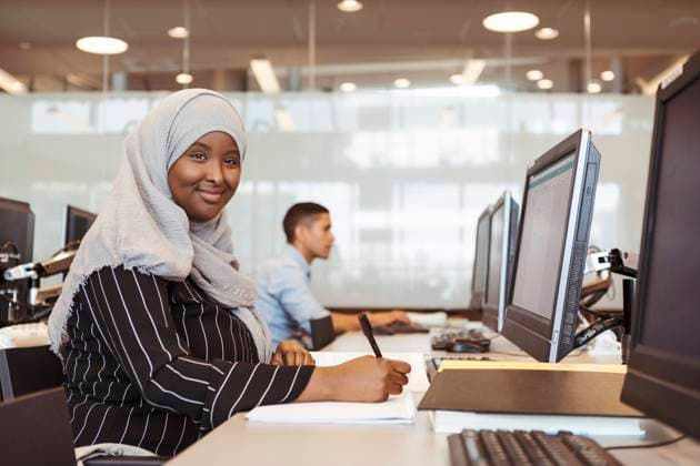 Portrait of smiling young female student writing in book while using computer at high school library , model released, property released Copyright: xKentarooxTrymanx , MA68331