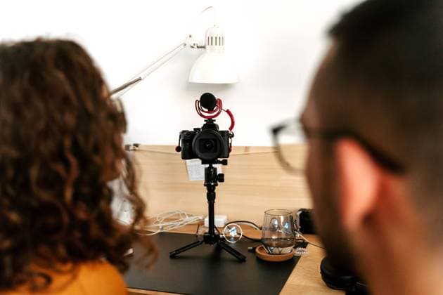 Back view of focused young couple blogger with curly hair in casual outfit and eyeglasses and professional photo camera placed on tripod while shooting video at home Copyright: xJakexJakabx Model Released