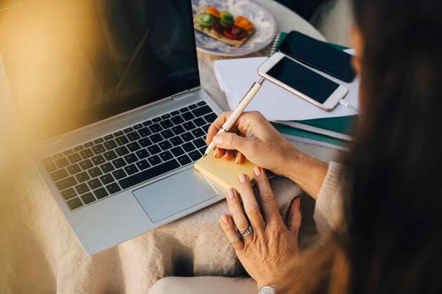 IMAGO Creative: Bildung, Schreiben Cropped woman writing on adhesive note over laptop at table , model released, property released Copyright: xMaskotx , MA68730