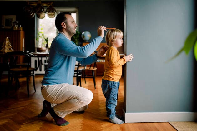 IMAGO Creative: Vaterschaft Full length of father measuring daughter s height against wall at home , model released, property released Copyright: xMaskotx , MA69036