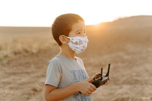 Side view of focused little Asian boy in protective mask using remote control while playing with flying drone in field Copyright: xJakexJakabx Model Released