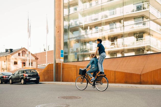IMAGO Creative: Stadt-Dichotomien Side view of young man riding bicycle with friend on street in city , model released Copyright: xMaskotx , MA69424