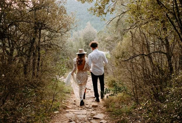 Back view of unrecognizable young bride and groom in stylish wedding outfits walking together on narrow stony path in mountainous forest in Morro de Labella in Spain, Model released Copyright: xJakexJakabx MR