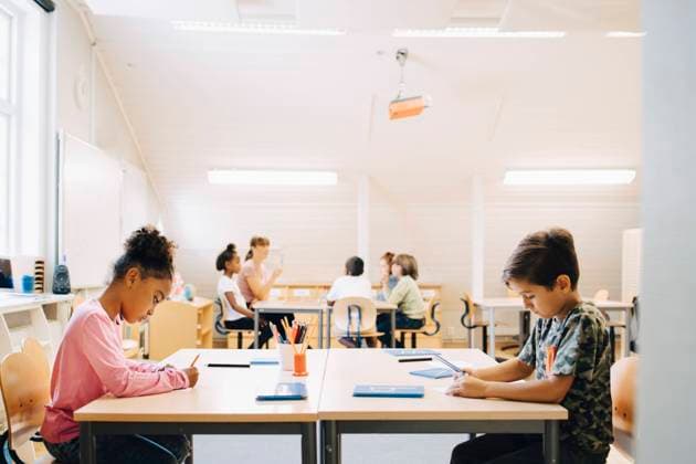 Boy and girl writing at desk while friends learning with student in background , model released, property released Copyright: xMaskotx , MA70236