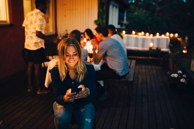 Smiling young woman using smart phone while friends in background at dinner party , model released, property released Copyright: xMaskotx , MA70301
