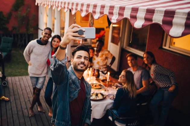 Smiling young man taking selfie with friends during dinner party , model released, property released Copyright: xMaskotx , MA70328