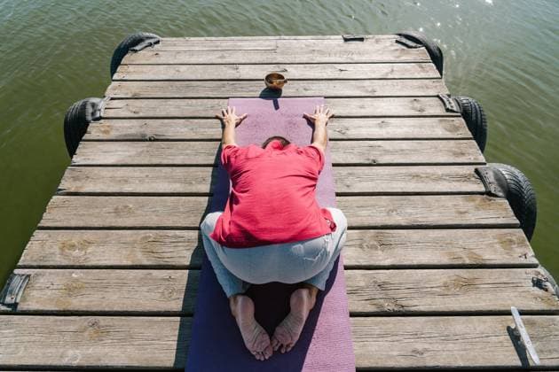 From above back view of anonymous male in casual clothes recreating in Extended Child pose during yoga session on wooden quay near sea on sunny day Copyright: xJavierxBallesterx Model Released