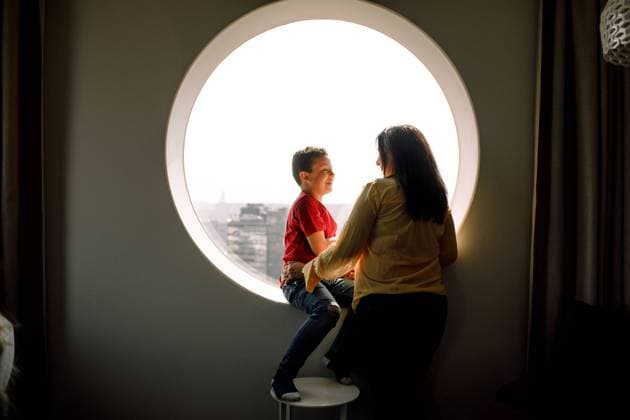 Smiling son looking at Mother while sitting on window in hotel room , model released, property released Copyright: xMaskotx , MA71635