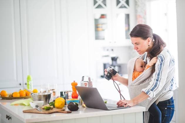 IMAGO Creative: Mutterschaft Side view of working mother food blogging while breastfeeding daughter in baby carrier at kitchen , model released, property released Copyright: xMaskotx , MA71890