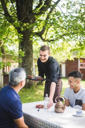 IMAGO Creative: Landleben - Essen Smiling young waiter talking with customers while working at outdoor cafe , model released, property released Copyright: xMaskotx , MA72979