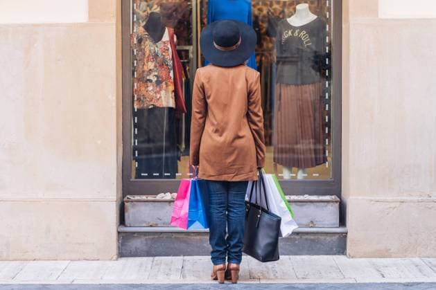 Back view of unrecognizable lady in stylish hat and brown jacket looking through shop window on fashionable dress with roses at city street Copyright: xJavierxDexLaxTorrex Model Released