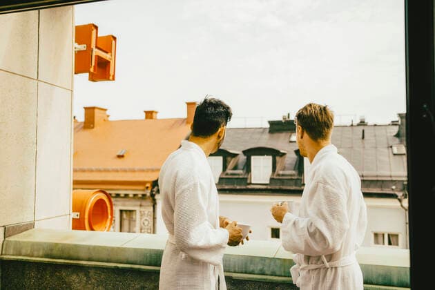 IMAGO Creative: Urban Diversity Gay couple in bathrobes holding coffee cups while standing at hotel balcony , model released, property released Copyright: xMaskotx , MA73362