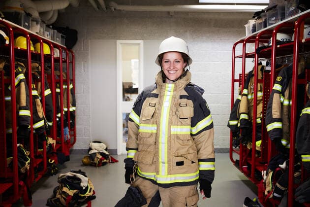 Portrait of smiling female firefighter standing in locker room at fire station , model released, property released Copyright: xMaskotx , MA73428