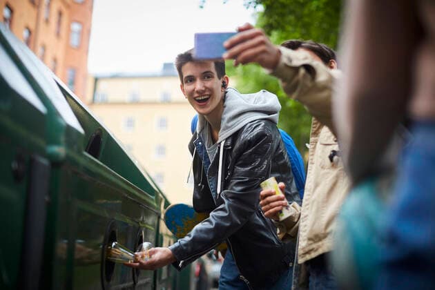 Man taking selfie with teenage friend throwing waste in garbage bin at recycling station , model released Copyright: xMaskotx , MA73757