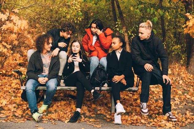 IMAGO Creative, Jahreszeit Herbst, Ferien Multi-ethnic friends looking at teenage girl using mobile phone while sitting on bench at park , model released Copyright: xMaskotx , MA74263