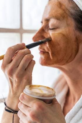 IMAGO Creative: Clickbait, Hautpflege und Kosmetik Side view of adult female standing with closed eyes in bathrobe and towel turban while putting hydrating cosmetic mask on face with brush Copyright: xJavierxDexLaxTorrex Model Released