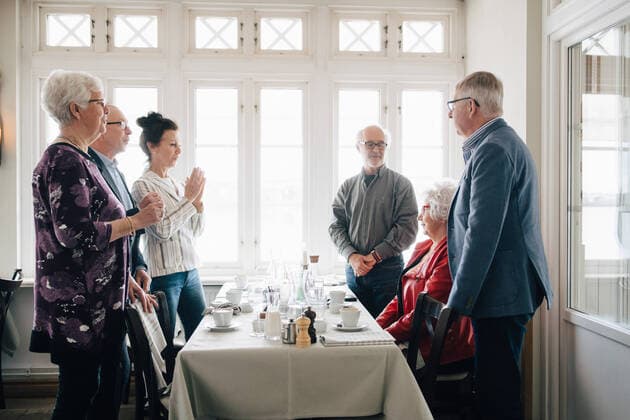 IMAGO Creative: Dichotomien, Reflexionen Senior woman sitting by restaurant table while male and female friends standing by table , model released, property released Copyright: xMaskotx , MA75009