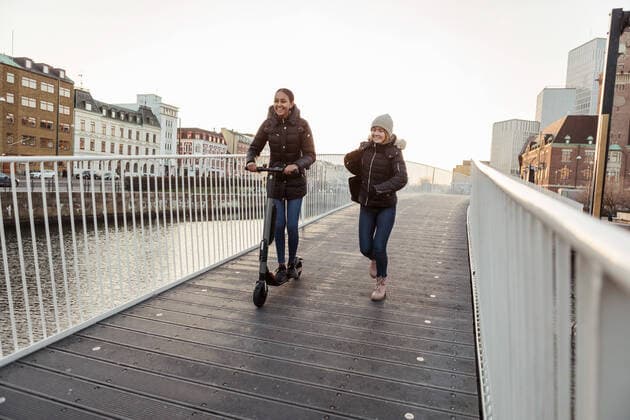 IMAGO Creative: Jahreszeit Winter, Spaziergang Happy female friends enjoying with electric push scooter on bridge in city , model released Copyright: xKentarooxTrymanx , MA75295