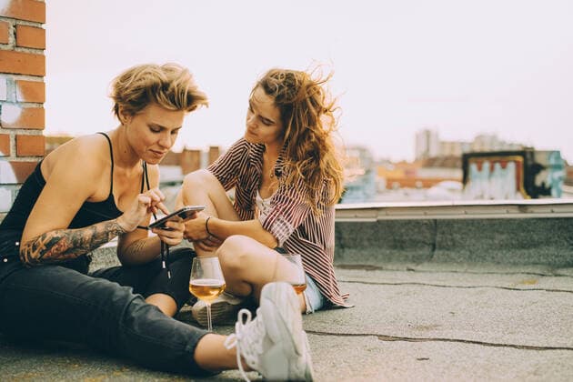 IMAGO Creative: Jahreszeit Frühling, Picknick Woman showing mobile phone to friend while sitting on terrace during rooftop party , model released, property released Copyright: xMaskotx , MA75612