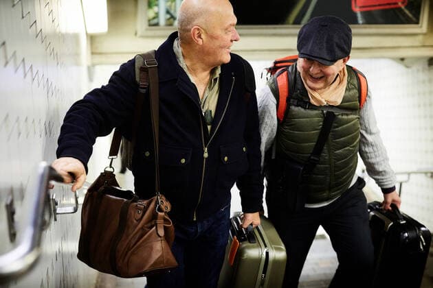 IMAGO Creative: Urban Diversity Smiling senior gay couple with luggage walking on staircase in subway , model released Copyright: xMaskotx , MA76569