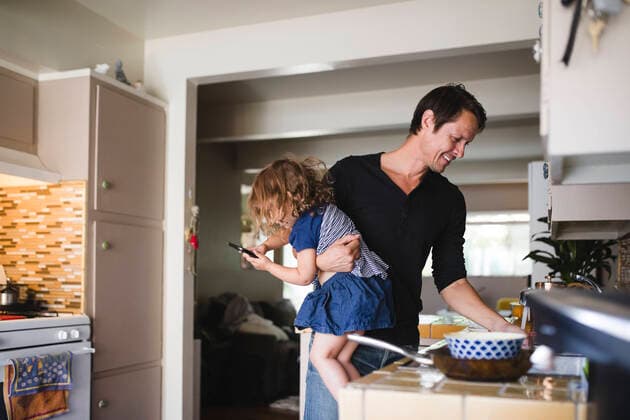 IMAGO Creative: Vaterschaft Daughter using phone while smiling father working in kitchen , model released, property released Copyright: xMaskotx , MA76699