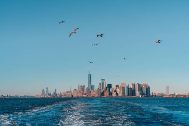 View from floating in water boat of Manhattan skyline with birds flying against blue cloudless sky, Model released Copyright: xJavierxMartinezx MR