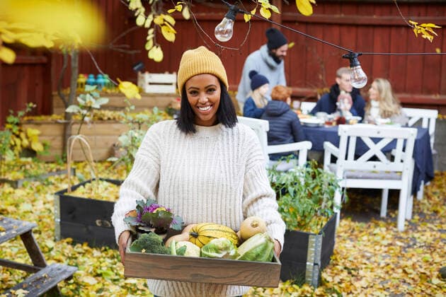 IMAGO Creative: Landleben - Essen Portrait of happy woman standing with vegetable basket while family and friends sitting at table in yard , model released, property released Copyright: xMaskotx , MA77134