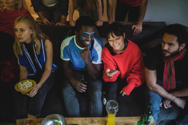 IMAGO Creative: Sport Start-Up Male and female using smart phone while sitting with friends on sofa at home , model released, property released Copyright: xMaskotx , MA77364