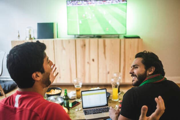 IMAGO Creative: Sport Start-Up Male friends talking while watching soccer in living room , model released, property released Copyright: xMaskotx , MA77379