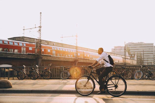 IMAGO Creative: Corporate: Klimaschutz, Digitalisierung und Urbanisierung Full length of businessman with backpack riding bicycle on road in city against sky , model released Copyright: xMaskotx , MA77508