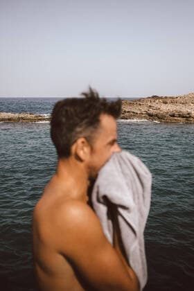 IMAGO Creative: Neue Aussichten Side view of man drying face with towel by sea on sunny day , model released Copyright: xMaskotx , MA77682