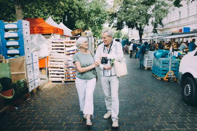 IMAGO Creative, Urban Lifestyle Full length of elderly couple talking while walking arm in arm at street market , model released Copyright: xMaskotx , MA78049
