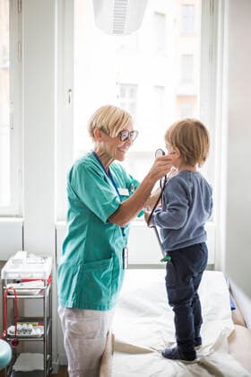Smiling female doctor holding stethoscope to boy s ear while standing in hospital , model released, property released Copyright: xMaskotx , MA78683