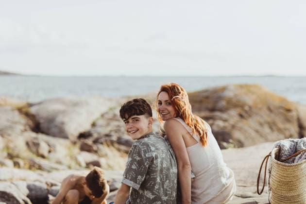 IMAGO Creative, Jahreszeit Sommer, Sommerferien Portrait of smiling mother and son bonding while sitting over rocky land during sunny day Sweden, Gothenburg, model released Copyright: xMaskotx , MA78864