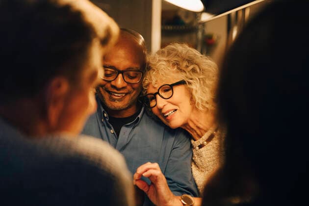 Smiling senior sharing smart phone with woman while sitting at illuminated dining table Sweden, Stockholm, model released, property released Copyright: xMaskotx , MA79973