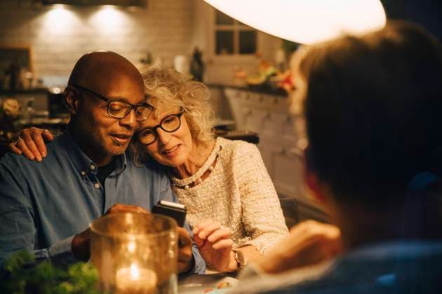 Bald senior sharing smart phone with woman while sitting at illuminated dining table Sweden, Stockholm, model released, property released Copyright: xMaskotx , MA79974