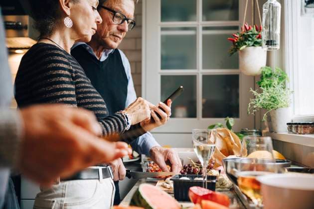 Senior woman showing smart phone to man while preparing dinner in kitchen Sweden, Stockholm, model released, property released Copyright: xMaskotx , MA80026