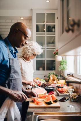 Multi-ethnic senior friends cutting fruits at counter while preparing dinner in kitchen Sweden, Stockholm, model released, property released Copyright: xMaskotx , MA80037