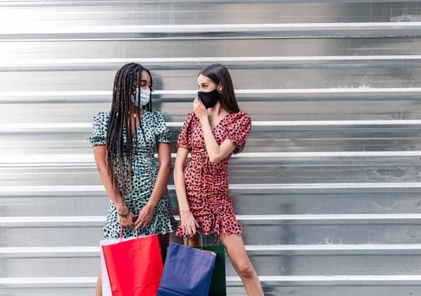 IMAGO Creative: Urban Diversity Multiethnic female friends in protective masks and similar dresses standing on street with paper bags after shopping and looking at each other, Model released Copyright: xJosexCarlosxGutierrezx MR
