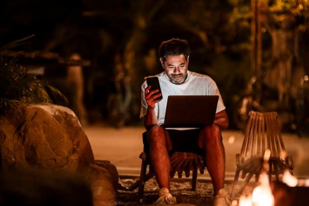 Smiling man with phone using laptop at night USA, California, model released Copyright: xMaskotx , MA80901