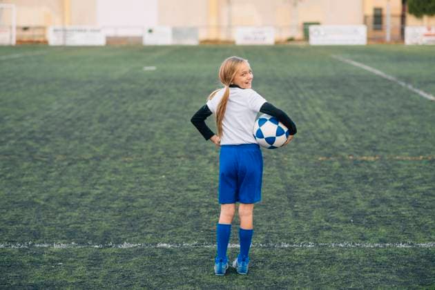 IMAGO Creative: Internationaler Frauenmonat, M?dchen im Sport Girl in white and blue uniform with soccer ball smiling at camera while standing alone on green field in modern sports club, Model released Copyright: xJosexLuisxCarrascosax MR
