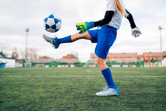 IMAGO Creative: Klub-Sport Low angle side view of unrecognizable teenage girl in white and blue uniform and goalkeeper gloves kicking ball while training alone in football arena at stadium in daytime, Model released Copyright: xJosexLuisxCarrascosax MR